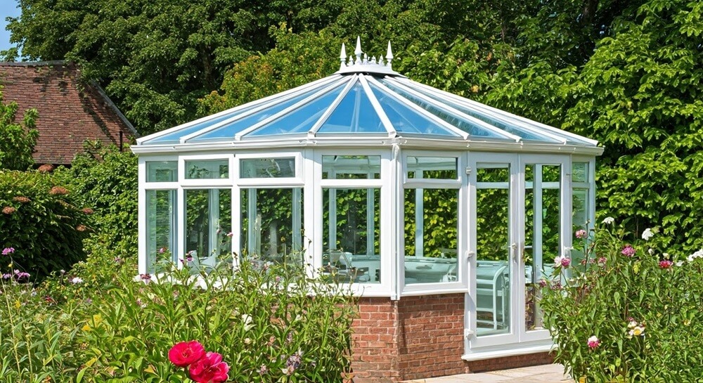 A white uPVC Energy-efficient conservatory in South Devon, surrounded by flowers, offering comfort and reduced heating costs year-round.